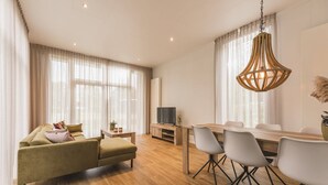 Un salon moderne comprenant un canapé, un pouf, une table à manger, des chaises et un téléviseur.