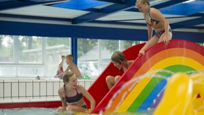 Une piscine avec un toboggan aux couleurs de l’arc-en-ciel et un espace aménagé au bord de la piscine.