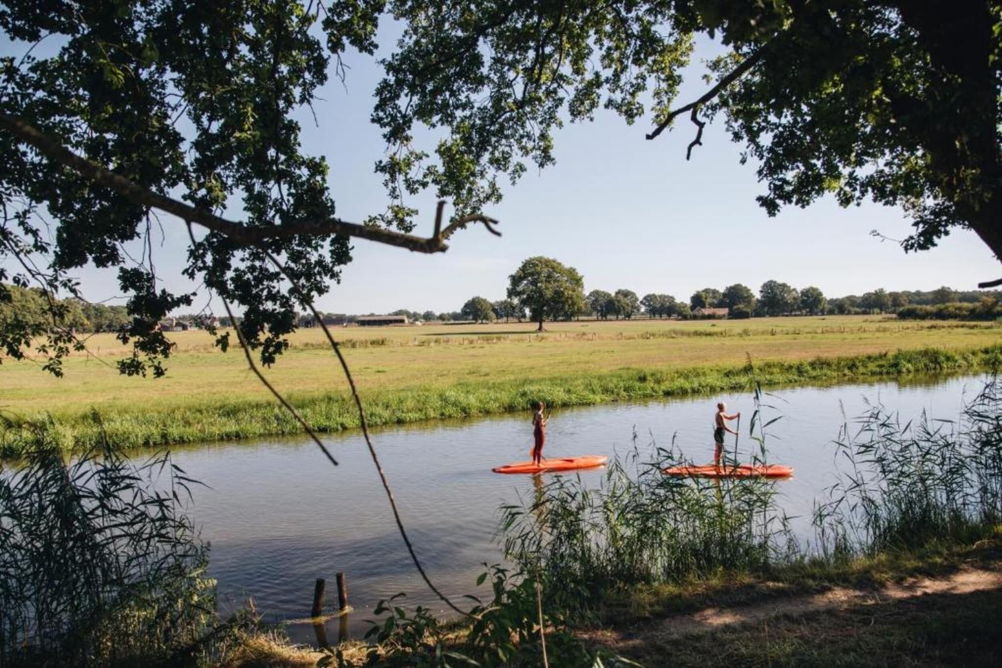 Ein Fluss, auf dem zwei Personen auf einem roten Stand-Up-Paddleboard paddeln.