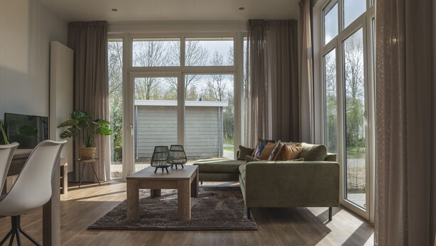 A spacious living room with a large window, a sofa, a coffee table, and a TV. - Holiday Home in Overijssel with Garden Terrace (Zuna)