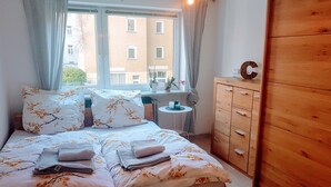 Une chambre à coucher avec un lit, une armoire en bois, une petite table ronde avec une lampe et une fenêtre avec des rideaux.
