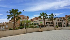 A spacious outdoor area with palm trees, a paved walkway, and modern buildings in the background. - NON STRESS First Level (Alboraya)