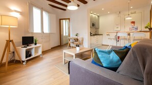 A modern living room with a sofa, a coffee table, and a TV on a stand. There is a kitchen area with a microwave and a dining table. - Fantastic and Bright Apartment in the Heart of Gothic area 10 min from the beach (Barcelona)