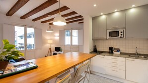 A modern kitchen with wooden beams, white cabinets, a wooden dining table, and a built-in microwave. - Fantastic and Bright Apartment in the Heart of Gothic area 10 min from the beach (Barcelona)