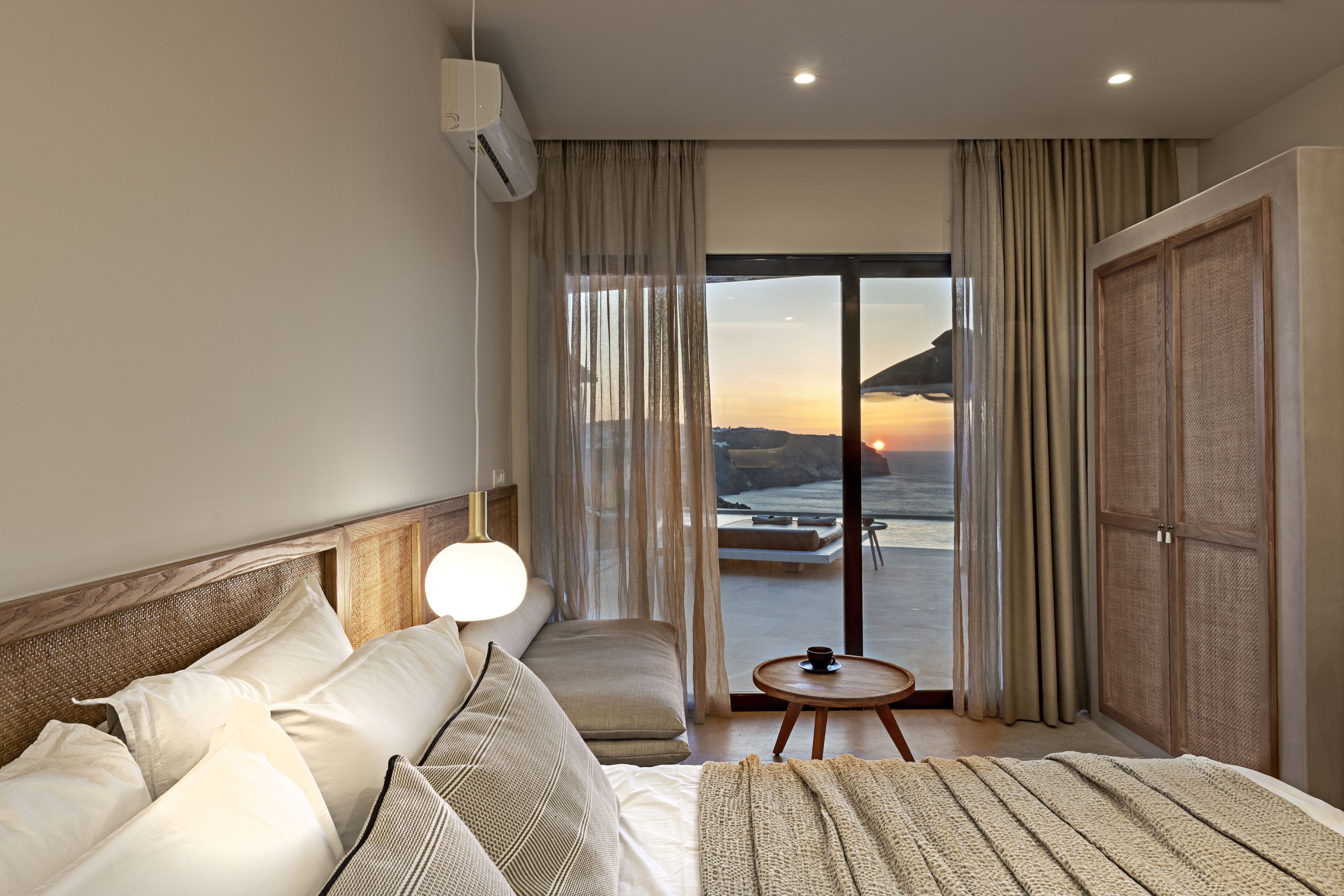 Habitación de hotel con una cama, un sofá, una mesita y vistas al atardecer a través de la ventana.