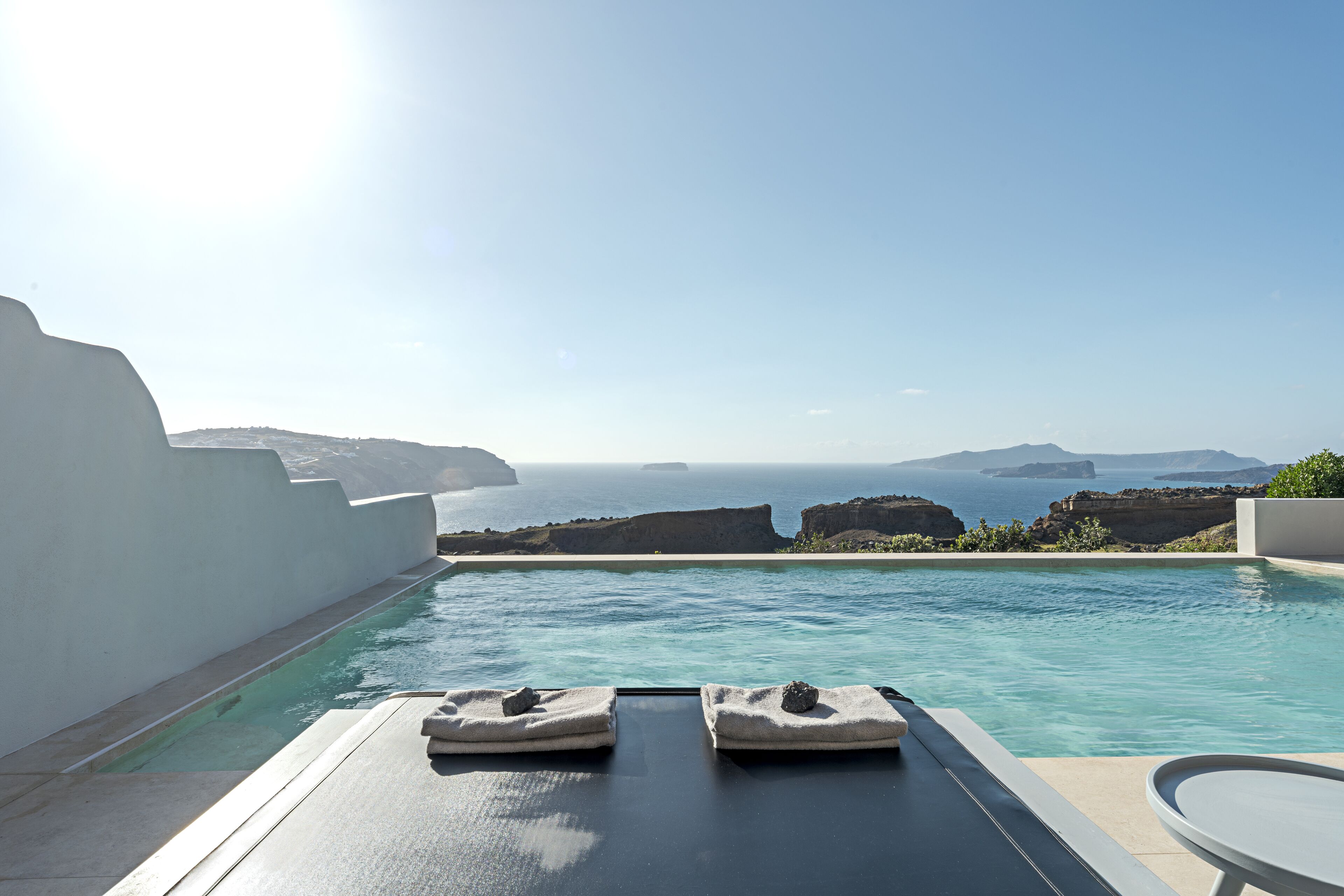A pool with two towels and a table, overlooking a scenic view of the sea and cliffs.