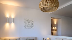 A modern living room with a grey sofa, a round white coffee table, and a woven pendant light. - Ambeli Sunset Villas (Santorini)