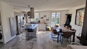 Moderni keittiö, jossa on ruostumattomasta teräksestä valmistetut kodinkoneet, keskellä oleva saareke baarituoleineen sekä ruokailutila, jossa on suuri pöytä ja tuolit.