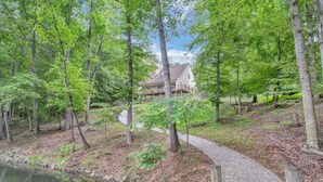 A wooded area with a stone pathway leading to a building with a covered deck. - Cozy Cove- Fenced yard for your dog and calm waters to swim for the family (Moneta)