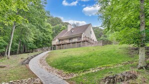A two-story house with a stone pathway leading to the entrance, surrounded by lush greenery and trees. - Cozy Cove- Fenced yard for your dog and calm waters to swim for the family (Moneta)
