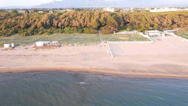 An aerial view of a beach with a sandy shore, a few structures, and a forested hill in the background. - Villa close to the sea with terrace and free parking  (Licinella-Torre di Paestum)