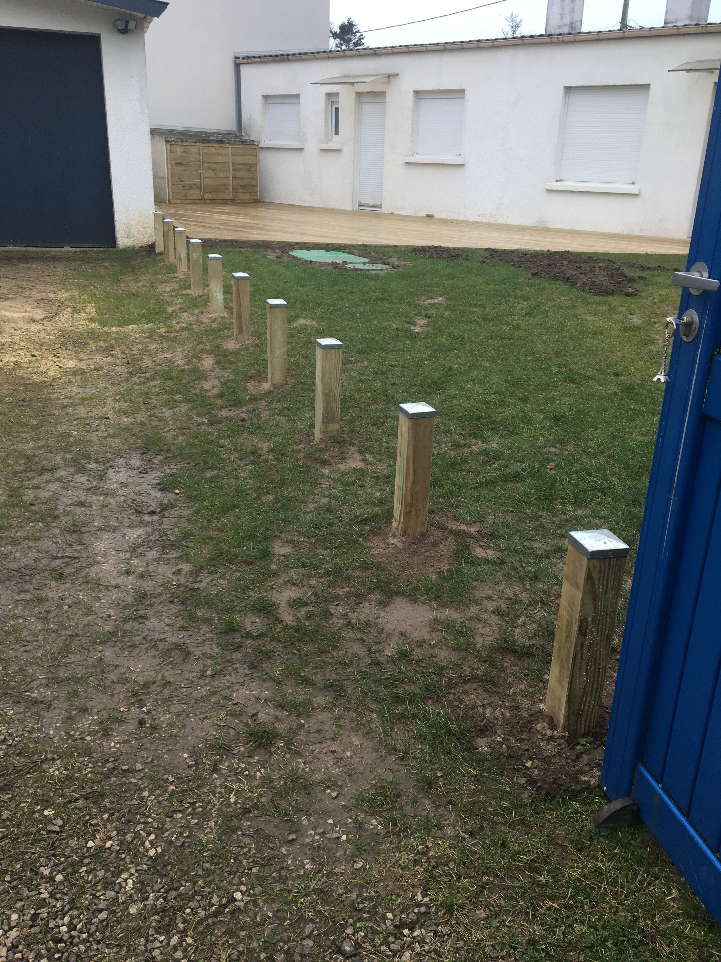 Een gazon met houten palen, een blauwe deur en een wit gebouw met ramen en een garage.