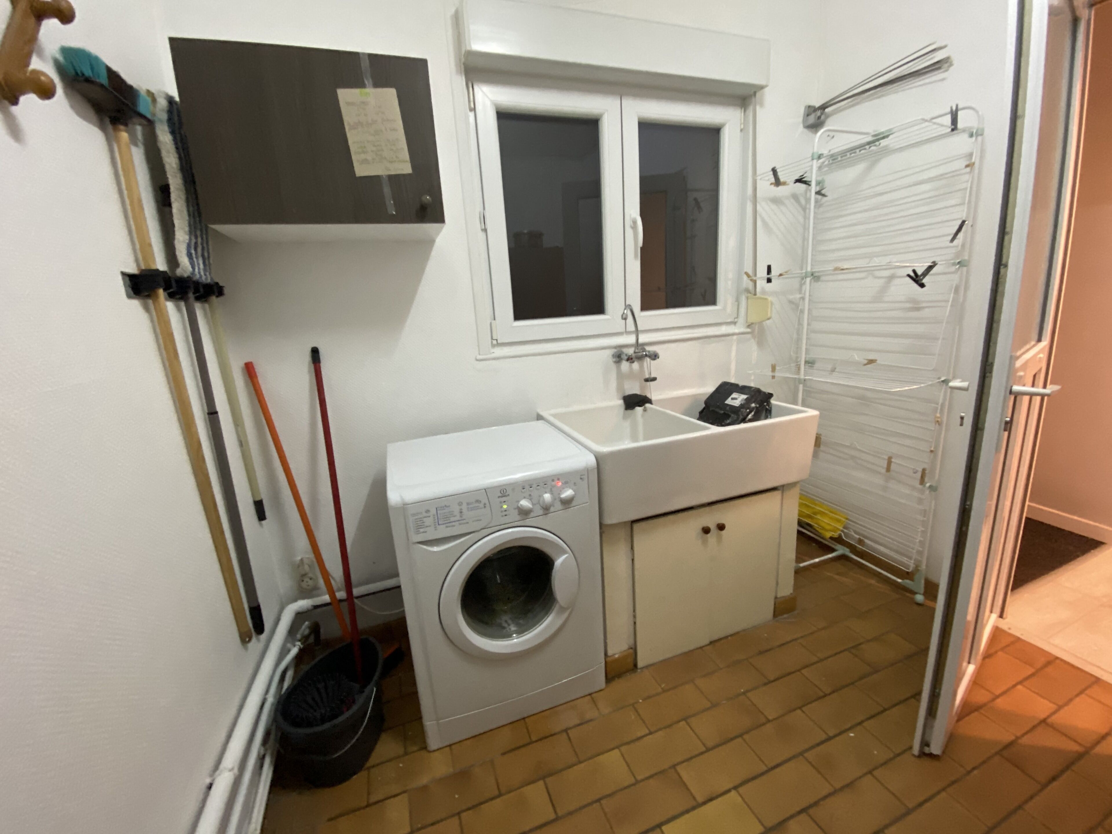 A compact laundry room with a washing machine, a sink, and a drying rack.