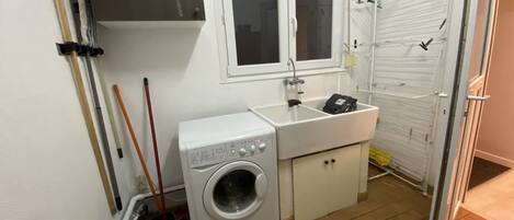 A compact laundry room with a washing machine, a sink, and a drying rack.