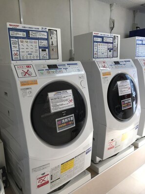 Une rangée de machines à laver blanches, dotées de panneaux de commande et d’instructions de sécurité.