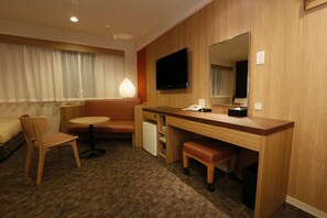 Habitación de hotel con un escritorio de madera, una silla, una mesita, un sofá, un televisor y un espejo.