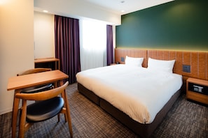 Habitación de hotel con una cama grande, un escritorio con silla y una mesita de noche.
