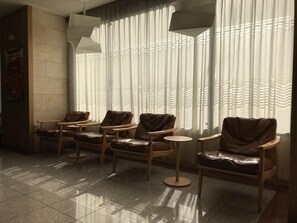 A waiting area with leather chairs and small tables, large windows with sheer curtains, and a tiled floor.