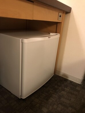 Un refrigerador Haier blanco y compacto en un rincón de una habitación, con una alfombra oscura de estampado y armarios de madera arriba.