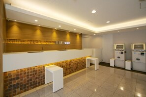 Un espace d’accueil comprenant un comptoir de réception, un panneau fixé au mur, un sol carrelé et une rangée de bornes en libre-service.