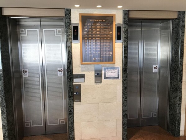 Un ascensor de hotel con un panel informativo digital que muestra los números de las habitaciones de huéspedes y una sala de reuniones.