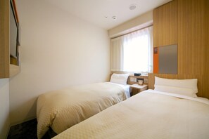 Habitación de hotel con dos camas, cabecera de madera, mesita de noche con lámpara y ventana con cortinas.