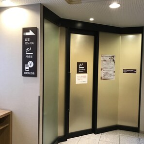 Entrada de un hotel con un letrero que indica las habitaciones de huéspedes y servicios como una sala para fumadores y una máquina expendedora.