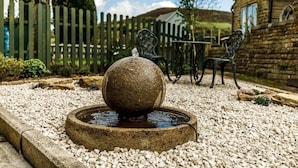 Une fontaine en pierre dans un jardin, avec une clôture en bois et des murs de pierre en arrière-plan.