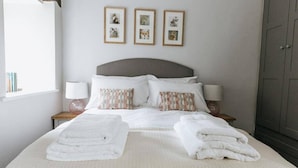 Un lit bien fait, avec du linge de lit blanc et deux oreillers, une table de chevet avec une lampe, et trois tableaux encadrés accrochés au mur.