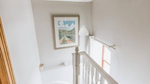 Un escalier avec une rampe blanche, un tableau encadré au mur et un luminaire suspendu.