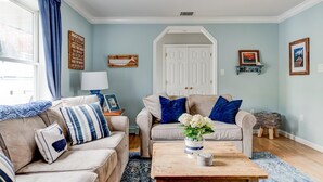 A living room with two beige sofas, a wooden coffee table, a blue rug, a lamp, and a door leading to another room. - Robeson Retreat (Sag Harbor)