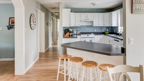 A modern kitchen with white cabinets, a granite countertop, and wooden stools. - Robeson Retreat (Sag Harbor)