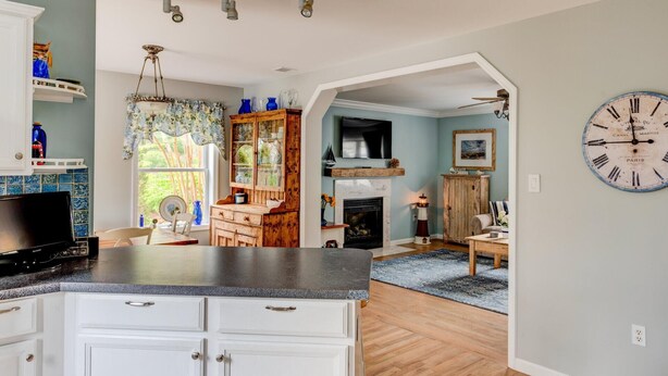A spacious kitchen with a large island, a dining area with a fireplace, and a living room with a clock on the wall. - Robeson Retreat (Sag Harbor)