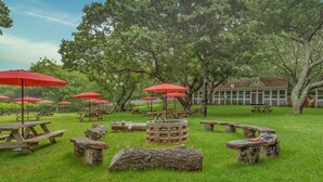 An outdoor area with picnic tables and red umbrellas, surrounded by trees. - Ruschmeyers #17 - Dlx King (Montauk)