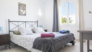 Una cama bien hecha con ropa de cama estampada, una mesita de noche, una lámpara y una ventana con cortinas.