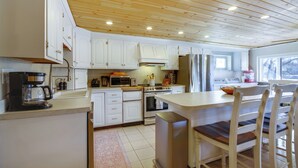 A kitchen with white cabinets, a wooden ceiling, and a dining area with wooden chairs.
