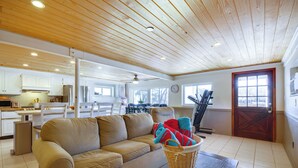 A spacious living area with a wooden ceiling, a beige sofa, a dining table, and a kitchen in the background.