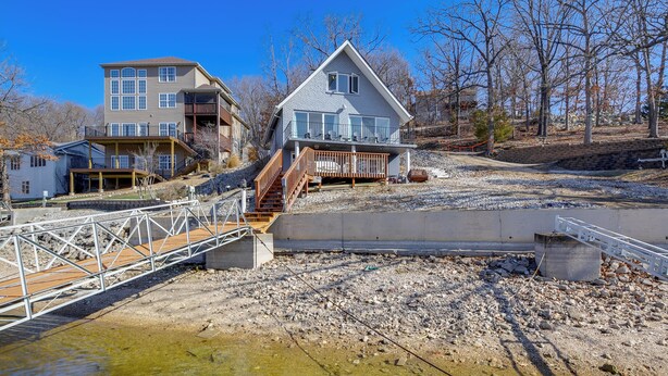 A two-story house with a balcony, a wooden deck, and a concrete bridge over a rocky area.
