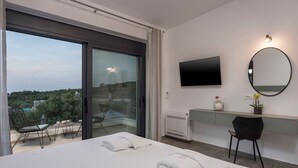 Ein Hotelzimmer mit Bett, Fernseher, Spiegel und einem Balkon mit Stuhl und Tisch.