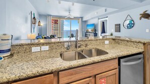Una cocina con encimeras de granito, pileta de acero inoxidable, muebles de madera y vista al exterior.