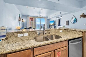 Una cocina con encimeras de granito, pileta de acero inoxidable, muebles de madera y vista al exterior.