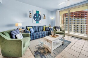 Una sala de estar con sofá, sillones, una mesa de centro y vista a un edificio a través de un ventanal.