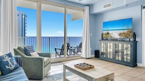 Un balcón con vista a la playa, un sofá, una mesa de centro y un mueble con televisor.
