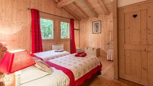 Een houten kamer met twee bedden, een raam met rode gordijnen, een radiator en een deur met een hartvormig uitsparing.