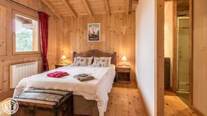 Een houten slaapkamer met een bed, twee nachtkastjes met lampen, een radiator, een raam met rode gordijnen en een poster aan de muur.