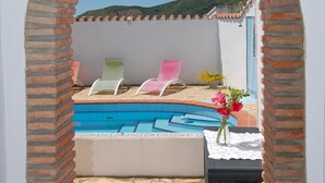 An outdoor swimming pool with a tiled deck, a brick archway, and a view of a mountain.