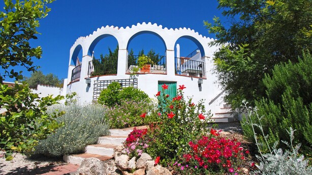 A white building with three arches, a green door, and a balcony with plants.