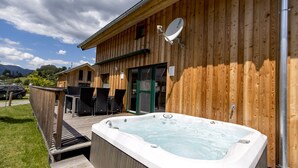A wooden building with a hot tub in front, a satellite dish on the roof, and a deck with chairs.
