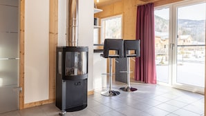 A modern kitchen with a wood stove, two bar stools, and a large window with a view of the mountains.