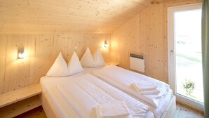 A wooden room with two beds, each with white linens and pillows, a heater, and a window with a view.